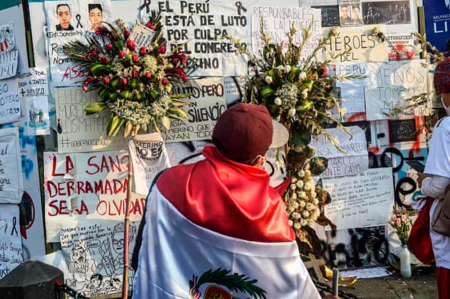 A man wearing a Peruvian flag stands in front of a mural in honour of Inti Sotelo and Bryan Pintado, two victims killed in recent protests.