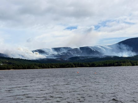 Smoke rises from hillsides next to a body of water