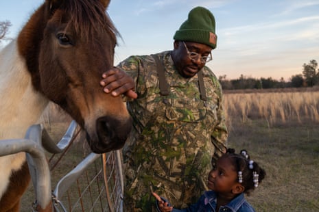 A man touching a horse with his young daughter looking on