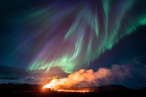 Northern lights play over erupting volcano