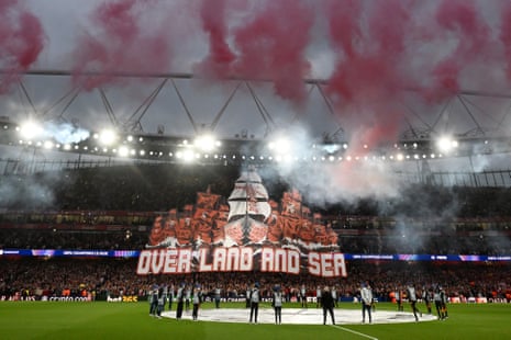 Οι οπαδοί της Άρσεναλ σηκώνουν ένα tifo που γράφει "Over Land and Sea" καθώς πραγματοποιείται επίδειξη πυροτεχνημάτων.