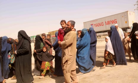 A line of women in burqas queue in the desert with children and men