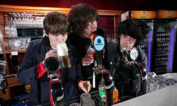 James Righton drinking from a tall mug of beer next to Jamie Reynolds with his mouth on a beer bottle and Simon Taylor-Davis of Klaxons at a bar