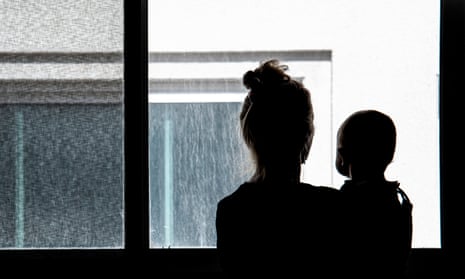 Silhouettes of woman and baby,looking out at featureless,concrete wall.