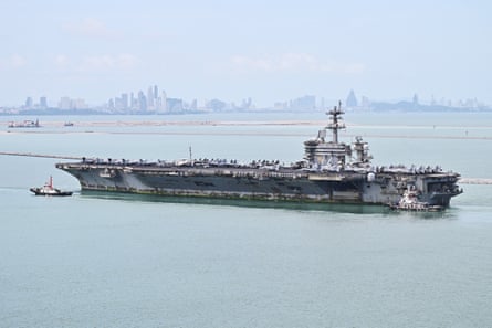 USS Abraham Lincoln surrounded by pale blue sea with a city in the background