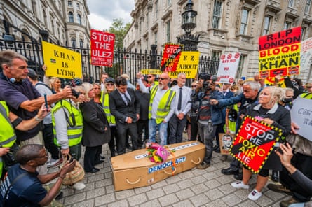 A group of protesters holding placards that read ‘Khan is lying’, ‘stop the Ulez’ and ‘RIP London’ stand around a coffin labelled ‘democracy’