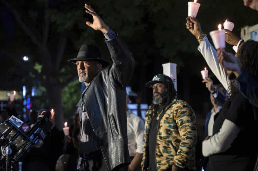 Sacramento: second suspect arrested as key questions go unanswered | California 1 A man standing at a bank of microphones holds his hand up in the air as people standing behind him holding candles with paper cup drip guards do the same.