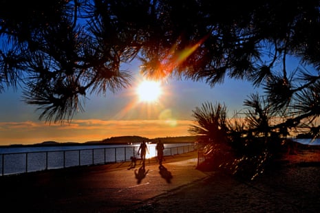 مردم در کنار آب قدم میزنند هنگام طلوع خورشید