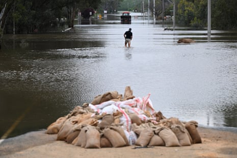 A man wades through flood water in Echuca with a pile of sand bags in the foreground