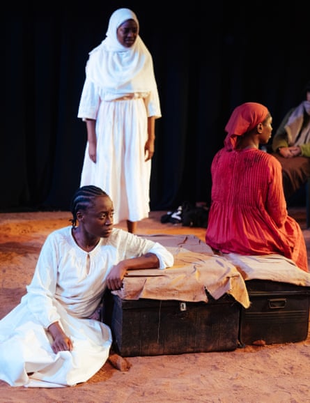 Two women of colour wearing white robes. One woman of colour wearing orange robes