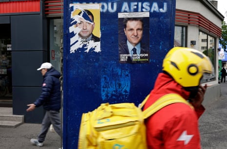 A food courier passes by a billboard displaying electoral posters of the candidates for the runoff of the 2025 presidential election, in Bucharest, Romania.