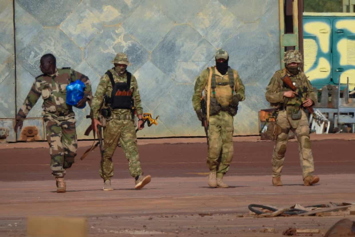 Four men in military camouflage outfits against a blue backdrop.