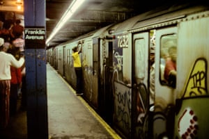 a Willy Spiller photo titled "Dangerous Ride, Boy Clinging Outside A Subway Car, 1977-1985" - a young man hangs on to the outside of a subway train as it stands at the station platform