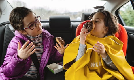 Cute carefree children enjoying doughnuts on the back seat of a car<br>Carefree siblings, sisters, enjoying their time together on the back seat of a car during a road trip.