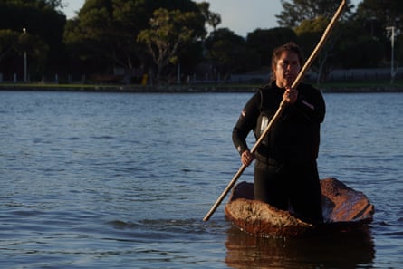 Tracey Rigney paddles a traditional bark canoe on calm water at twilight