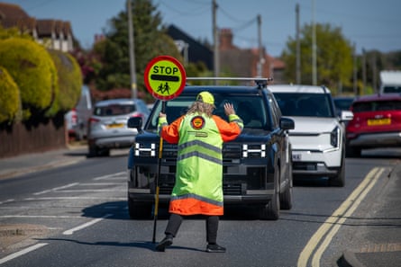 She stands in front of traffic with her hand raised, wearing her lollipop uniform and holding her stop sign