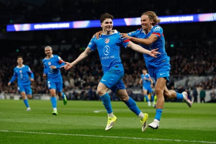 Julián Alvarez of Atlético Madrid, wearing all blue kit and yellow boots, celebrates with teammates after scoring against Tottenham.