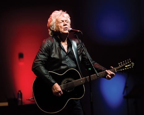 An older man plays acoustic guitar and sings.