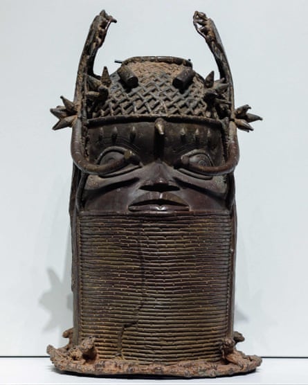 A Benin bronze sculpture of a warrior with a helmet and a long lined covering from the neck to the lips