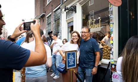 A man takes a picture with his phone of two tourists posing outside Fabel Friet, a chip shop popularised on TikTok