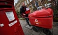 A man pushes a red letter-carrying wagon next to a post box
