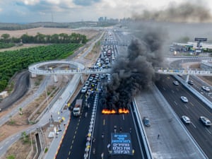 Three lanes of traffic backed up as far as the eye can see behind a line of burning tyres
