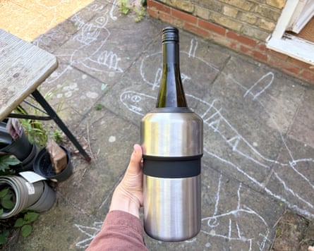 A bottle of wine in a Huski wine cooler held above a garden patio.