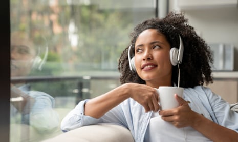 Woman at home drinking coffee while listening to something through headphones