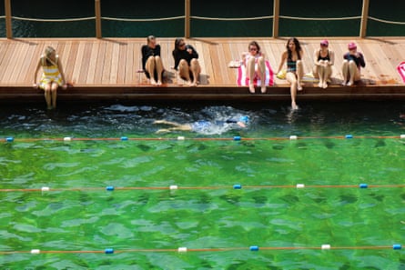 Bathers loll on a boardwalk by the lanes of an open air swimming pool