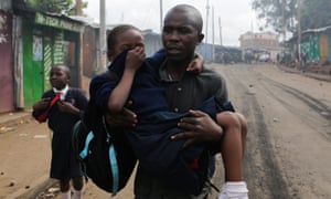 A man carries a schoolgirl overcome by tear gas and smoke from burning barricades during running battles between police and protesters in the Kibera slum of Nairobi.