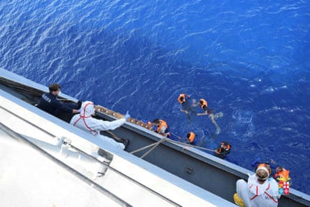 People on an Italian navy vessel pulls refugees aboard