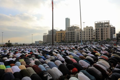 Large crowd of people bow in prayer outside a mosque.