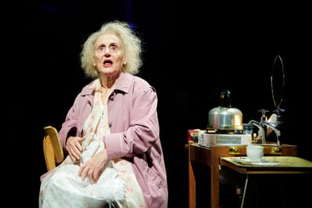 An elderly woman wearing a nightie under a purple jacket looks frightened.