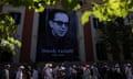 People queue beneath a giant picture of Ismail Kadare wearing sunglasses, marked with his life dates, 1936-2024