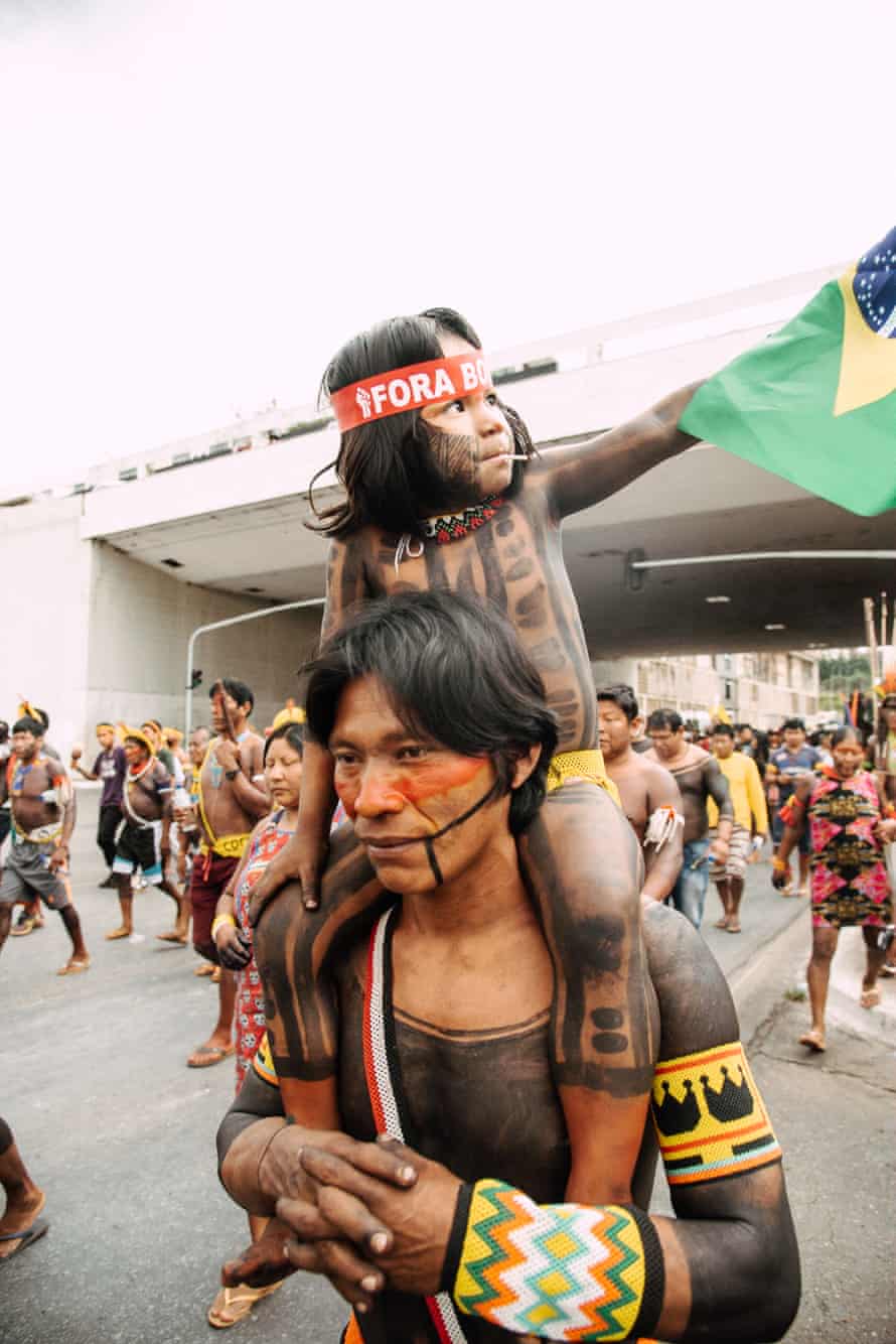 An indigenous man marches with his daughter on his shoulders.