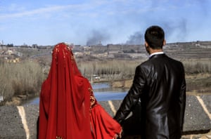 A couple hold hands for a wedding photograph as they view smoke rising over the district of Sur, Turkey
