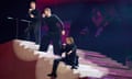 The three members of Take That dressed in black at various levels of a white staircase on stage.