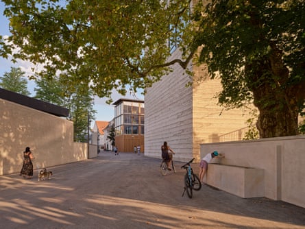 A lane leads to Zumthor’s Erlen Torhaus office and art-handling block, with a fountain in the foreground that a woman is drinking from