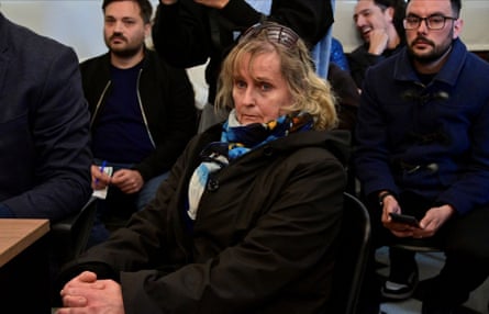 Patricia Kadgien sits in a chair wearing a big black coat surrounded by officials