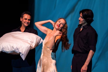 A woman poses with her arms raised while standing in between two men dressed in black.