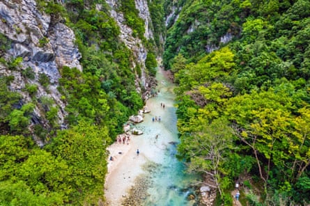 Aerial view of the Acheron springs - pale blue water and a few people standing on white sand in a lush gorge