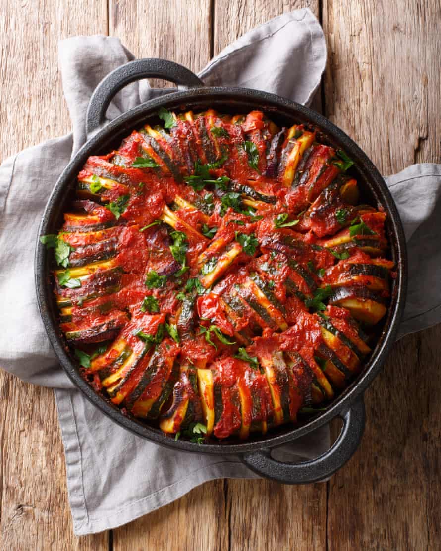 Baked zucchini, potatoes, eggplant and onions in tomato sauce close-up in a pan.