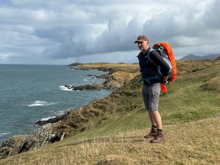 A man standing on a grassy cliff overlooking the sea.