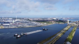 Four boats transport a tunnel section along a waterway