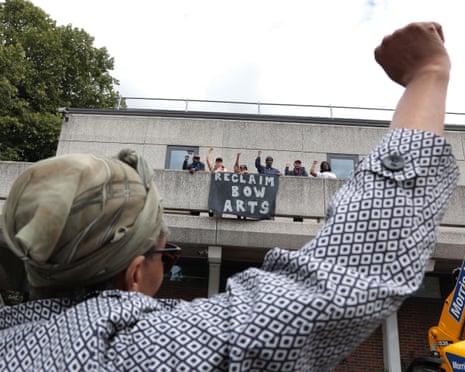 A woman raises her first in defiance as others do the same on a balcony of the estate, with a sign hanging off the balcony saying 'Reclaim Bow Arts'
