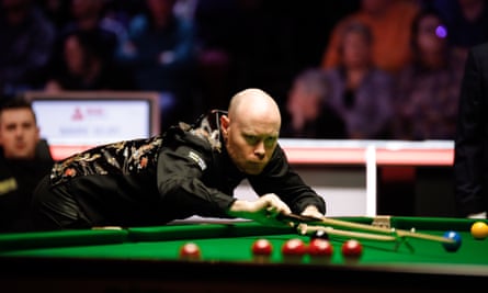 Gary Wilson, wearing a black waistcoat adorned with an oriental pattern, leans on the edge of the snooker table as he plays a shot at Manchester Central 