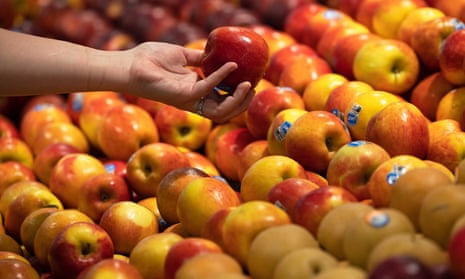 Eine Hand hält einen Apfel, der aus Apfelreihen in einem Supermarkt gepflückt wurde.