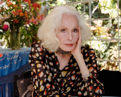 An older woman in a patterned blouse leans her face on one hand.