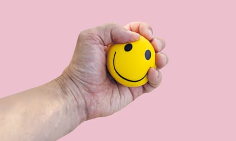 A hand squeezing a stress ball with a smiley face on it