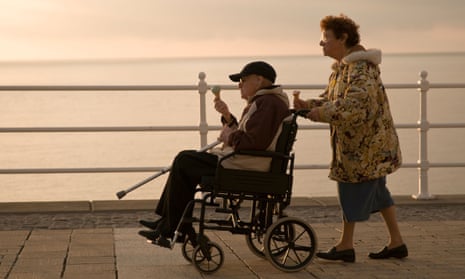 Elderly woman pushing her husband in a wheelchair on a summer evening by the sea